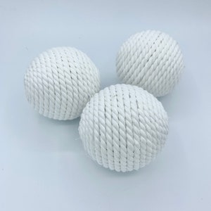 Puede incluir: Tres bolas de cuerda blancas, cada una hecha de cuerda blanca tejida apretadamente, est&aacute;n dispuestas sobre una superficie blanca.