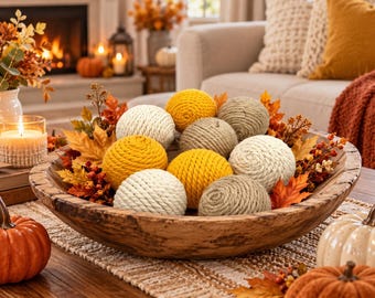 May include: A large, round, wooden bowl filled with decorative spheres wrapped in yellow, cream, and beige rope. The bowl is arranged with artificial autumn leaves, orange berries, and small pumpkins, creating a seasonal display of textures.