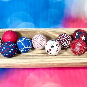 May include: A wooden bowl filled with red, white, and blue fabric balls. The balls have various patriotic patterns, including stars, stripes, and fireworks.