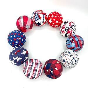 May include: A set of ten fabric balls in red, white, and blue with various star and plaid patterns. The balls are arranged in a circle.