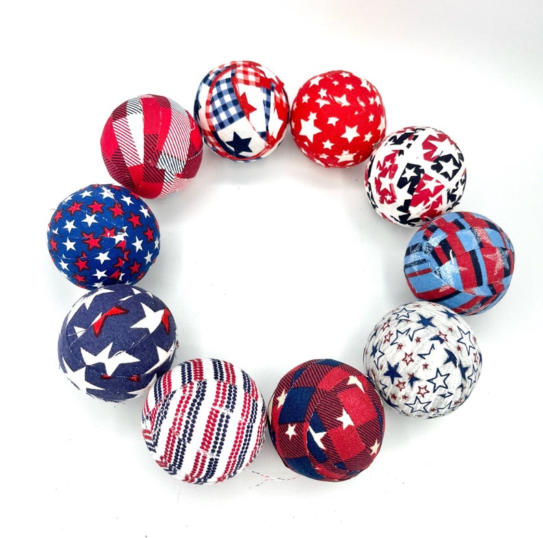 May include: A set of ten fabric balls in red, white, and blue with various star and plaid patterns. The balls are arranged in a circle.