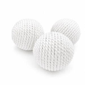 May include: Three white decorative spheres made of tightly wound rope. The spheres are arranged in a cluster, with two in the background and one in the foreground. The rope has a textured appearance, and the spheres are set against a white background.