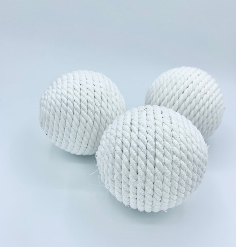 Puede incluir: Tres bolas de cuerda blancas, cada una con una textura tejida, est&aacute;n dispuestas sobre una superficie blanca. Las bolas son de forma ovalada y parecen estar hechas de fibras naturales.