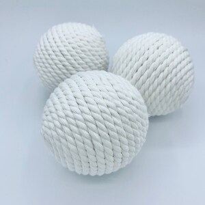 Puede incluir: Tres bolas de cuerda blancas, cada una hecha de cuerda blanca tejida apretadamente, est&aacute;n dispuestas sobre una superficie blanca.