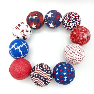 May include: A circle of nine fabric-covered balls in red, white, and blue patriotic colors. The balls have different patterns, including stars, stripes, and polka dots.