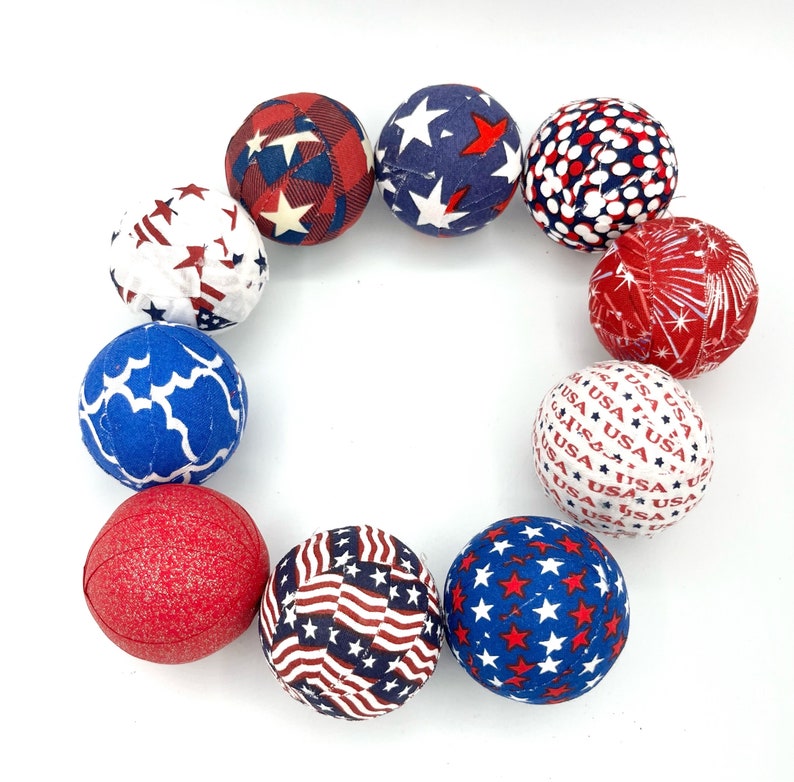 May include: A circle of nine fabric-covered balls in red, white, and blue patriotic colors. The balls have different patterns, including stars, stripes, and polka dots.