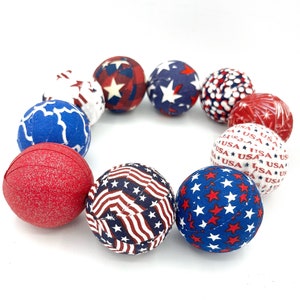 May include: A circle of red, white, and blue fabric balls with various patriotic patterns. The balls are decorated with stars, stripes, and the word "USA".