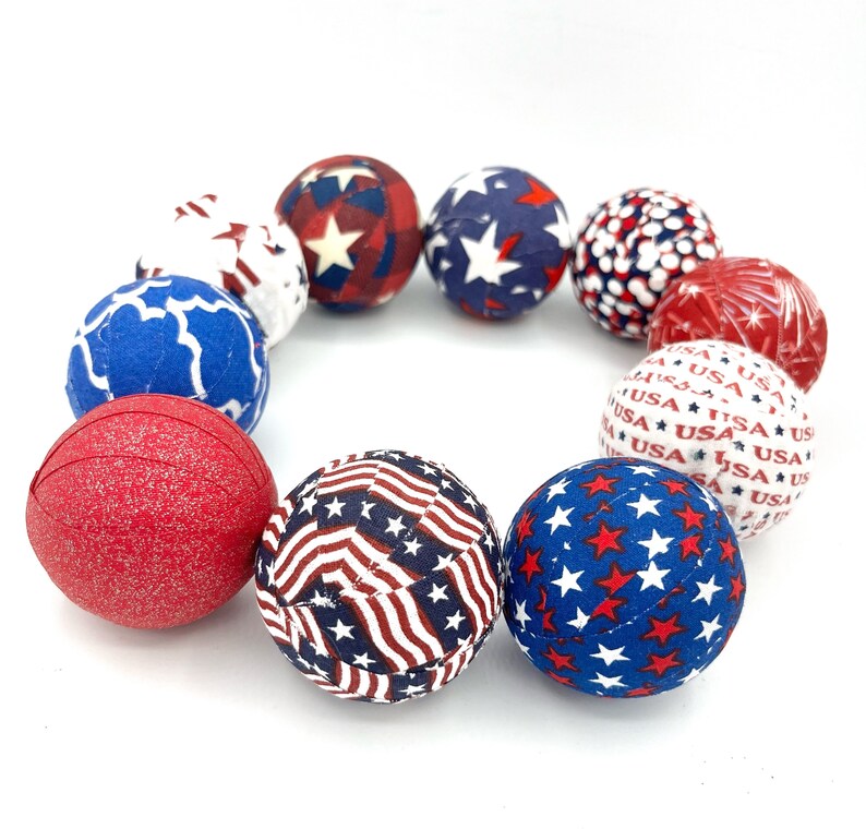 May include: A circle of red, white, and blue fabric balls with various patriotic patterns. The balls are decorated with stars, stripes, and the word "USA".