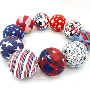 May include: A set of ten fabric-covered balls in red, white, and blue with various star and stripe patterns. The balls are arranged in a circle.