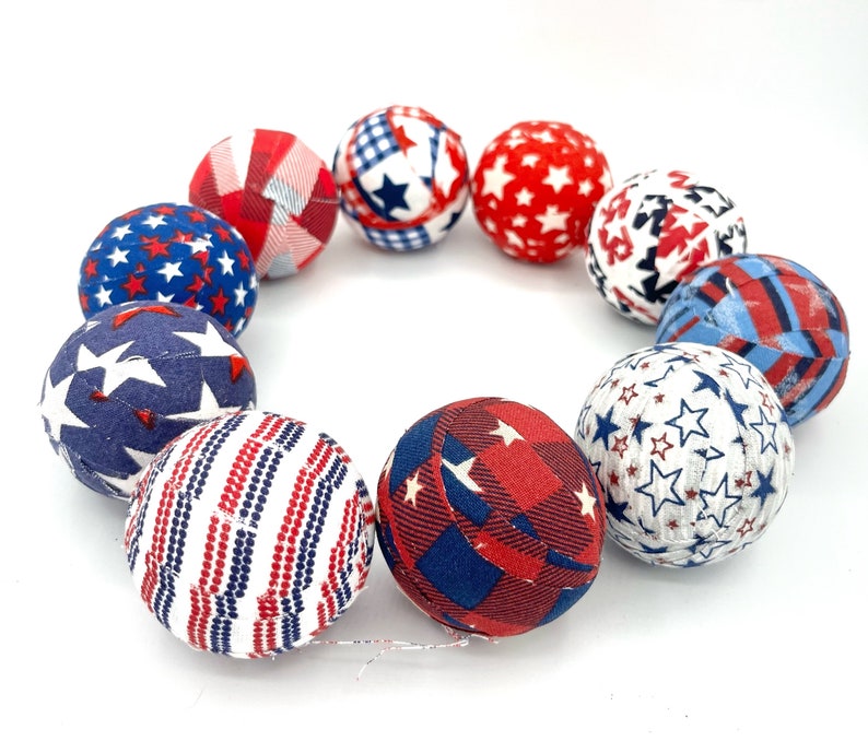May include: A set of ten fabric-covered balls in red, white, and blue with various star and stripe patterns. The balls are arranged in a circle.