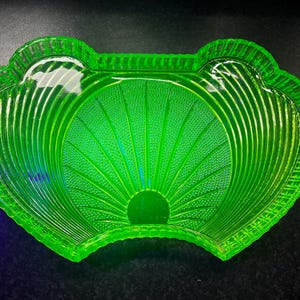May include: A bright green glass dish with a scalloped edge and a textured, fan-like pattern. The dish has a central circular base and vertical ribbed detailing, creating a striking visual effect. The glass has a bright, almost neon, appearance.