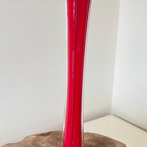 Pode incluir: Um vaso alto e esguio de vidro vermelho com uma base transparente e alargada. O vaso tem uma forma longa e cilíndrica que se afunila ligeiramente para cima. A cor vermelha é vibrante e brilhante, e a base transparente adiciona um toque de elegância.
