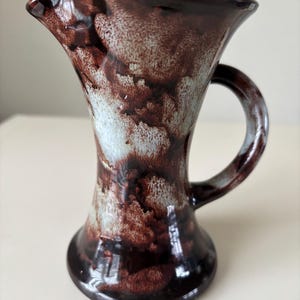 May include: A small brown and white ceramic jug with a marbled glaze. The jug has a wide mouth and a handle.