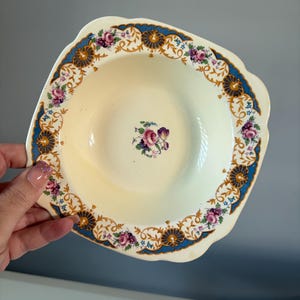 May include: A white ceramic bowl with a blue and gold floral design. The bowl has a scalloped edge and a slightly raised center.
