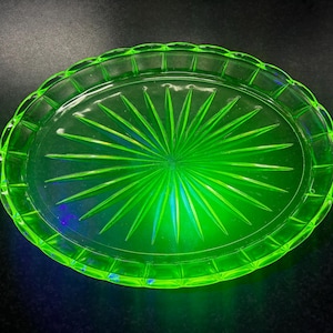 May include: A vibrant green, oval-shaped glass serving tray. The tray features a sunburst design in the center and a scalloped edge. The tray measures approximately 10 inches in length and 7 inches in width.