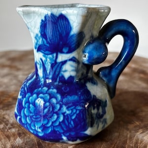 Puede incluir: Una taza de cerámica blanca con un asa negra y el texto "But First, Coffee" en negrita negra. La taza se encuentra sobre un fondo borroso, resaltando su diseño limpio.