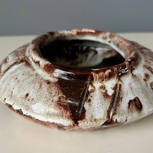 May include: A white ceramic ashtray with brown glaze and a textured surface.