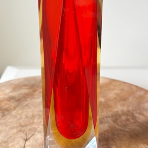 Könnte beinhalten: Eine rechteckige Vase aus rotem und gelbem Glas mit einem klaren, facettierten Boden. Die Vase hat eine hohle, längliche Form mit einem leuchtend roten Innenraum und gelben Akzenten. Die Vase ist etwa 25 cm hoch.