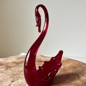 Puede incluir: Una taza de cerámica blanca con un asa negra y el texto "But First, Coffee" en negrita negra. La taza está sobre una superficie de madera. La taza mide 10 cm de alto.