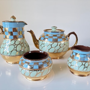 May include: A vintage tea set with a light blue, gold, and mint green color scheme. The set includes a teapot, creamer, sugar bowl, and a coffee pot. The pieces have a gold trim and handles, and a checkered and oval pattern.