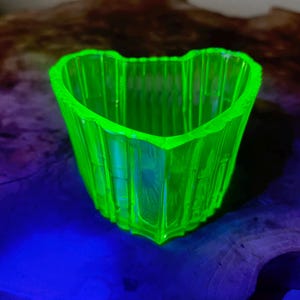 May include: A vibrant, neon green glass heart-shaped dish. The dish features a textured, ribbed pattern and glows brightly. This decorative item is likely vintage or antique. The dish is a unique piece.