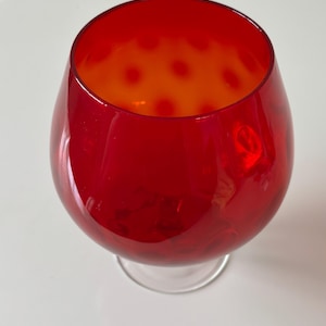 May include: A large, red glass goblet with a clear, circular base. The interior of the goblet has an orange hue with red polka dots. The glass has a glossy finish and is likely used for beverages.