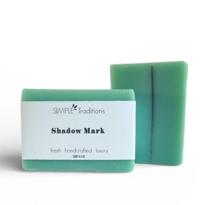 May include: Two rectangular, green soap bars. One bar has a white label with the text "SIMPLE Traditions" and "Shadow Mark". The other bar is a solid green color. The soap is labeled as fresh, handcrafted, and luxury.