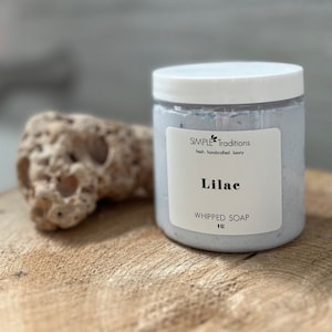 Peut inclure: Un pot blanc de savon fouetté parfumé à la lilas avec un couvercle blanc. Le pot est étiqueté "SIMPLE Traditions" et "WHIPPED SOAP 11oz".