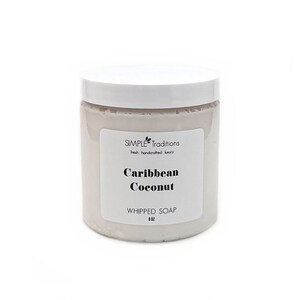 May include: A cylindrical container of light pink whipped soap with a white lid. The label reads Simple Traditions, fresh. handcrafted. luxury, Caribbean Coconut, WHIPPED SOAP, and 8 OZ. The container is opaque and has a smooth, matte finish.