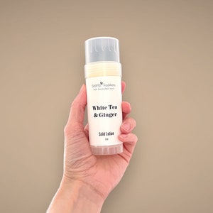 May include: A white tube of solid lotion with a white label that says "SIMPLE traditions" and "White Tea & Ginger" in black text. The label also says "Solid Lotion" and "2 oz" in black text.