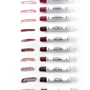 K&ouml;nnte beinhalten: Eine Auswahl an Lippenfarben in verschiedenen Farbt&ouml;nen, darunter Courageous Dreamer und Berry Blush. Jede wei&szlig;e Tube hat einen dunklen Deckel und einen Farbabstrich. Der Text "SIMPLE Traditions" ist auf jeder Tube zu sehen.