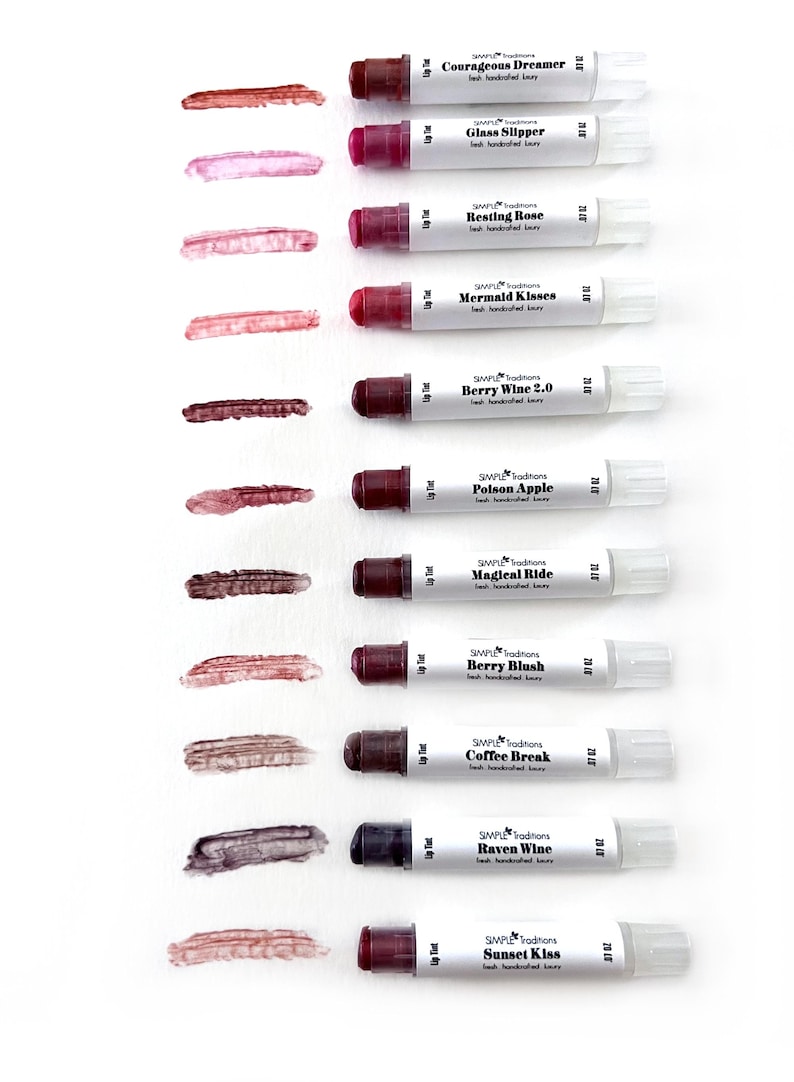 K&ouml;nnte beinhalten: Eine Auswahl an Lippenfarben in verschiedenen Farbt&ouml;nen, darunter Courageous Dreamer und Berry Blush. Jede wei&szlig;e Tube hat einen dunklen Deckel und einen Farbabstrich. Der Text "SIMPLE Traditions" ist auf jeder Tube zu sehen.