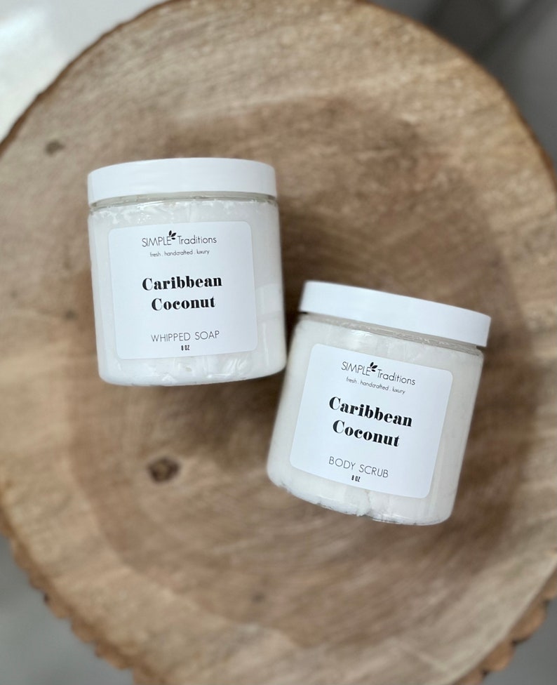 May include: Two white jars with black labels. The labels read "SIMPLE Traditions" and "Caribbean Coconut". One jar is labeled "WHIPPED SOAP" and the other is labeled "BODY SCRUB".