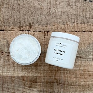 May include: A white plastic jar of Caribbean Coconut whipped soap with a white lid and a label reading Simple Traditions, Caribbean Coconut, WHIPPED SOAP, 8 oz, alongside an open jar revealing the white, textured, creamy soap contents.