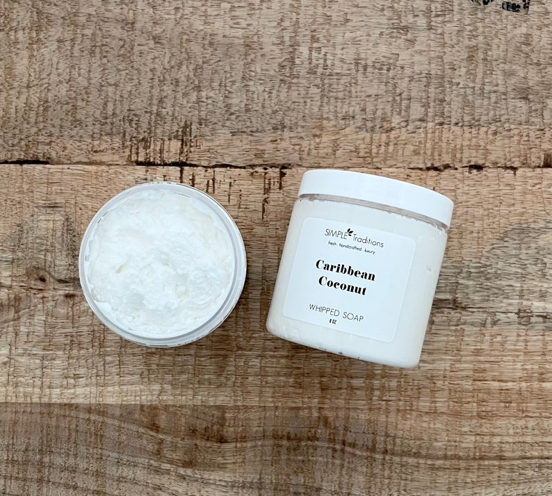 May include: A white plastic jar of Caribbean Coconut whipped soap with a white lid and a label reading Simple Traditions, Caribbean Coconut, WHIPPED SOAP, 8 oz, alongside an open jar revealing the white, textured, creamy soap contents.