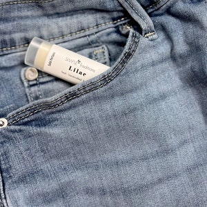 Pu&ograve; includere: Un tubetto bianco di profumo solido con la scritta "SIMPLE Traditions Lilac fresh handcrafted" sull'etichetta. Il tubetto &egrave; in una tasca di jeans blu.
