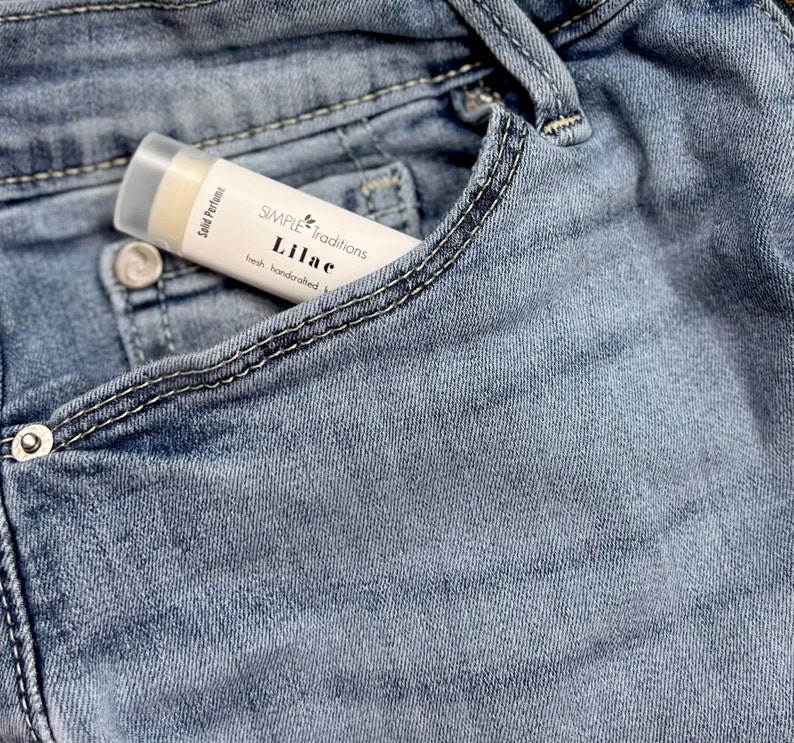 Pu&ograve; includere: Un tubetto bianco di profumo solido con la scritta "SIMPLE Traditions Lilac fresh handcrafted" sull'etichetta. Il tubetto &egrave; in una tasca di jeans blu.