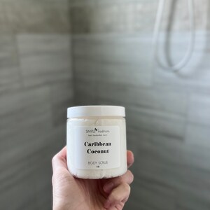 May include: A white jar of body scrub with a black label that reads "SIMPLE Traditions fresh handcrafted luxury Caribbean Coconut BODY SCRUB 4 oz."