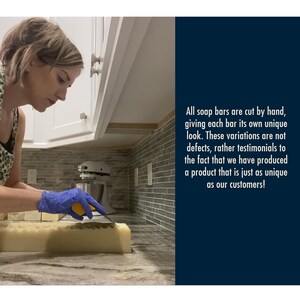 May include: A person wearing blue gloves cuts a bar of handmade soap with a knife. The soap is light yellow and has a rough texture. The text in the image reads: "All soap bars are cut by hand, giving each bar its own unique look. These variations are not defects, rather testimonials to the fact that we have produced a product that is just as unique as our customers!"