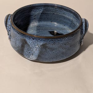 May include: A blue and black speckled ceramic baking dish with two handles. The dish has a brown rim.