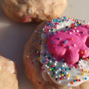 Op de afbeelding: Close-up van glazuurkoekjes met kleurrijke hagelslag en roze glazuur. De koekjes hebben een lichtbruine basis en zijn bedekt met witte glazuur en een roze decoratieve vorm. De hagelslag is veelkleurig.