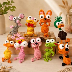 May include: A collection of nine small, handmade crochet animal figures featuring a gray mouse, a yellow creature with a red bow tie, an orange cat, a green duck, a yellow bird, a pink panther-like figure, a pink dog, a green frog, and an orange fox.