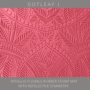 May include: A pink rubber stamp mat with an intricate design of leaves and dots. The design is symmetrical and features a repeating pattern. The mat is labeled "DOTLEAF I INTAGLIO FLEXIBLE RUBBER STAMP MAT WITH REFLECTIVE SYMMETRY".