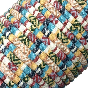 May include: A close-up of a spool of colorful patterned fabric cord. The cord is made of woven cotton and features a variety of colors, including yellow, blue, red, and green. The cord is tightly wound around the spool, creating a visually appealing pattern.