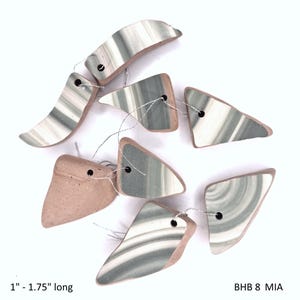 May include: Ceramic beads in various shapes, strung with silver thread. The beads are primarily white, gray, and tan, with a striped pattern. Each bead is between 1 and 1.75 inches long.