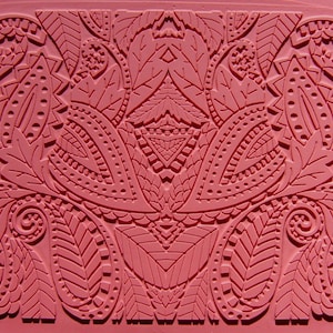 May include: A pink silicone mold with a detailed, intricate design of paisley patterns and leaves. The mold is designed for creating decorative items like cake toppers or soap.