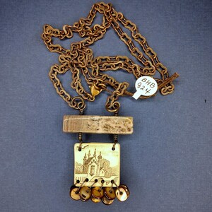 May include: A handmade necklace with a bronze chain and pendant. The pendant includes a rectangular stone, a square ivory-coloured piece with a church illustration, and dangling circular charms. The necklace has a tag that reads "BHB 824".