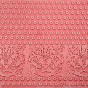 May include: A red rubber doormat with a repeating pattern of small circles. The bottom edge of the mat features three embossed images of a cat's face.