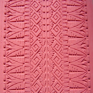 Könnte beinhalten: Ein rosa Stempel aus Gummi mit einem geometrischen Muster. Das Muster zeigt ein sich wiederholendes Muster aus Quadraten, Dreiecken und Linien.