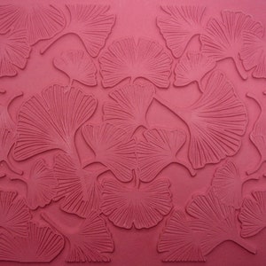May include: A textured, reddish-pink surface featuring a repeating pattern of ginkgo leaf designs. The leaves are embossed, creating a raised relief effect. The ginkgo leaves are fanned out with detailed veining, adding depth and visual interest to the design.